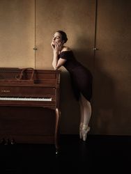 Graceful ballerina leaning on top of piano standing on tiptoe