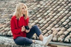 Woman sitting atop rocky stoop in Spanish town with SLR camera