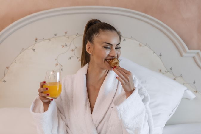 Woman in bathrobe eating breakfast in bed in a hotel room