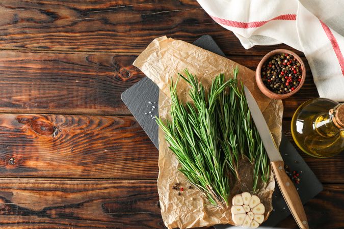 Composition with rosemary, oil, pepper, garlic and knife on wooden table, top view