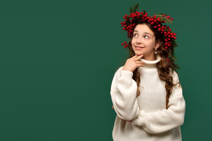 Smiling girl in festive red berry wreath looking thoughtfully.