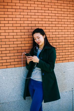 Asian female listening to music near brick wall