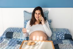 Cheerful pregnant woman speaking on smartphone during breakfast