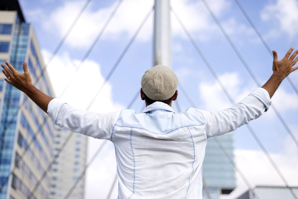 Male in denim standing with outstretched arms on bridge