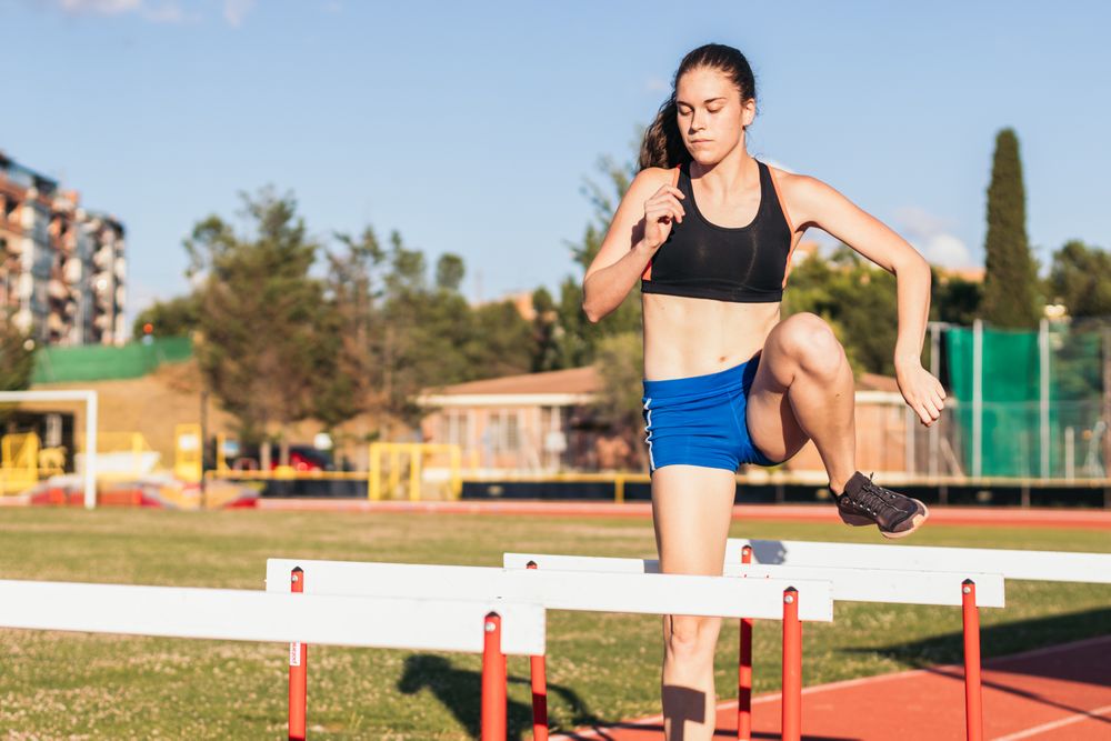 athlete training by jumping hurdles on an athletics track.