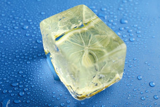 Top view of large rectangular ice cube with lemon slice on blue table