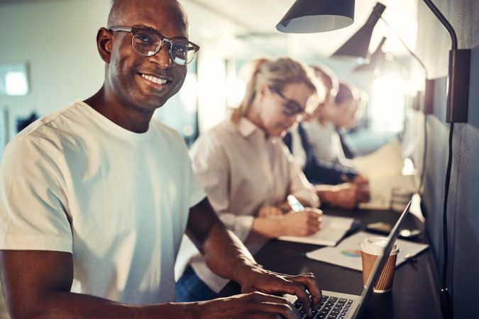 Man smiling while working on his laptop in an open office