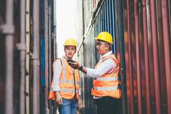 Asian container worker talking on walkie talkie to control work quality at dock
