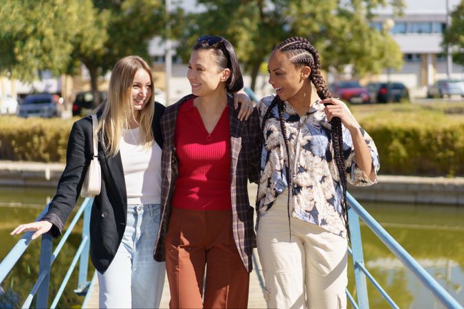 Three women walking over pedestrian bridge on sunny day