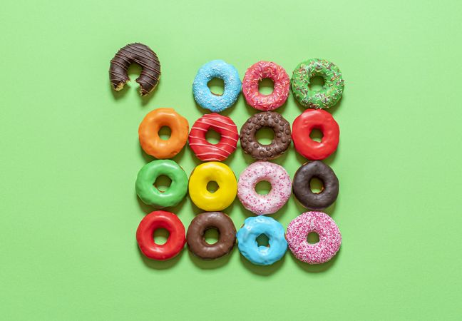 Chocolate donuts with multicolored icing, top view on a green background