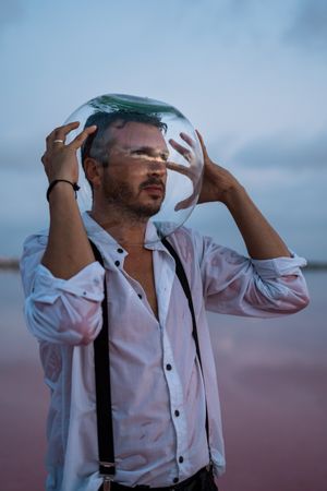 Man with fish tank on head standing at seashore