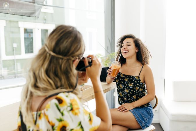 Woman taking photo of friend in cafe