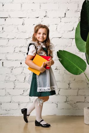 Full-length portrait adorable little schoolgirl in uniform in front of brick wall