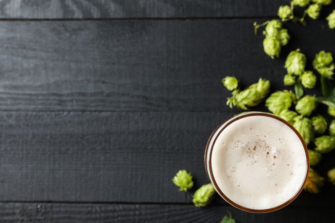 Glass of beer and hop cones on wooden background, top view