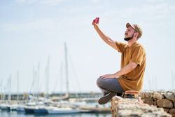 Man with a cap sitting relaxed on a skateboard taking a self-portrait