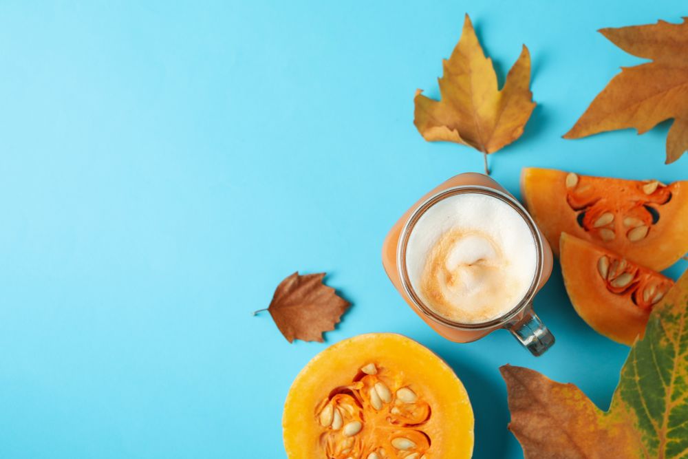Composition with glass jar of pumpkin latte on blue background