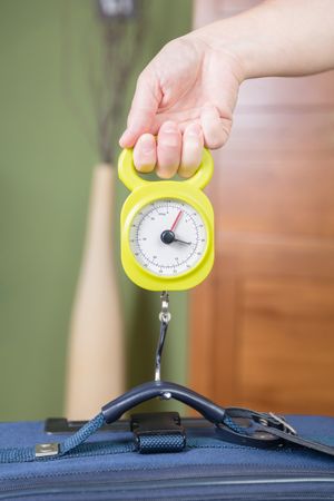 Woman checking luggage weight with a hand balance