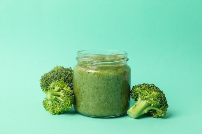 Glass jar with broccoli puree on mint background