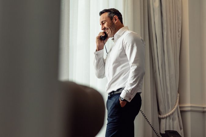 Businessman smiling and talking on phone from hotel room