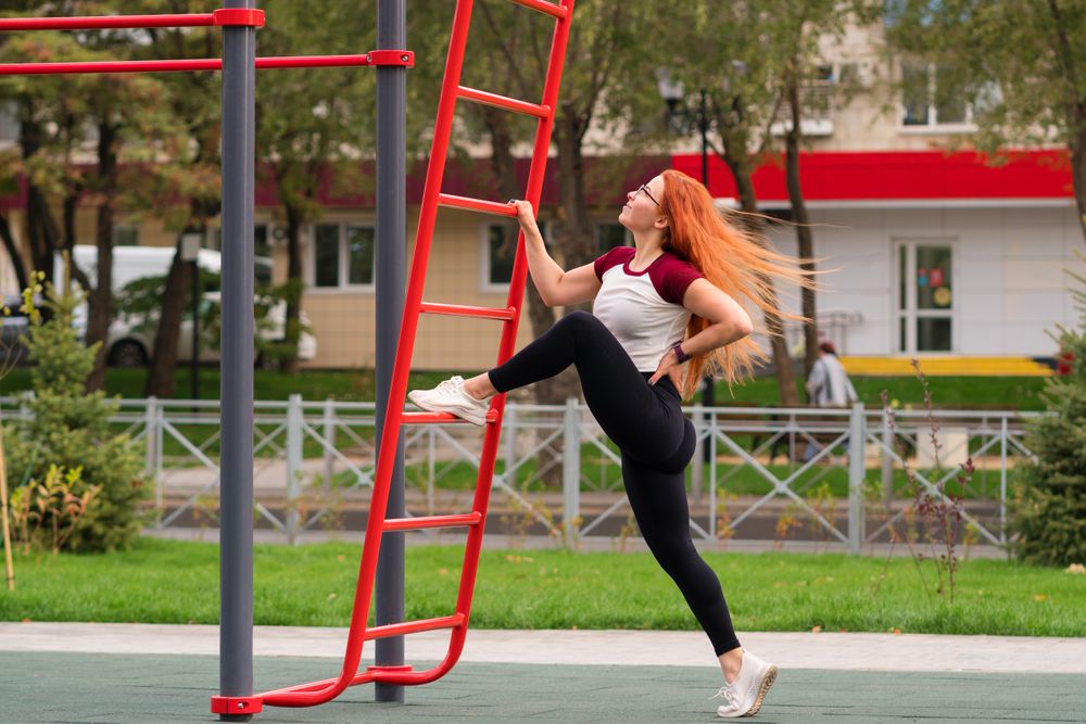 Woman stretching leg with hand on outdoor equipment