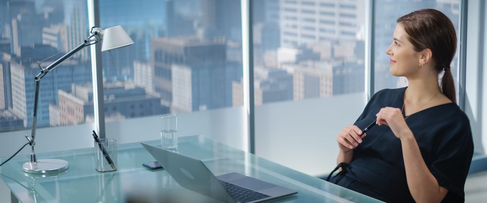Portrait of Young Successful Businesswoman Sitting at Desk Working on Laptop Computer in City Office.