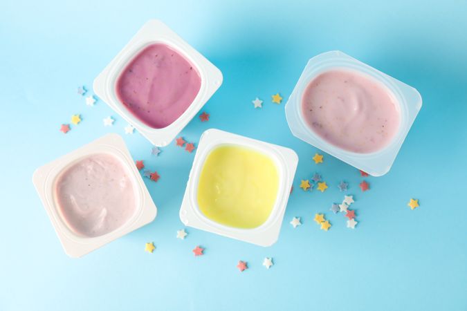 Plastic cups with yogurt and small stars on color background, space for text
