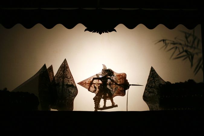 Layered shadow puppet figure holding a shield