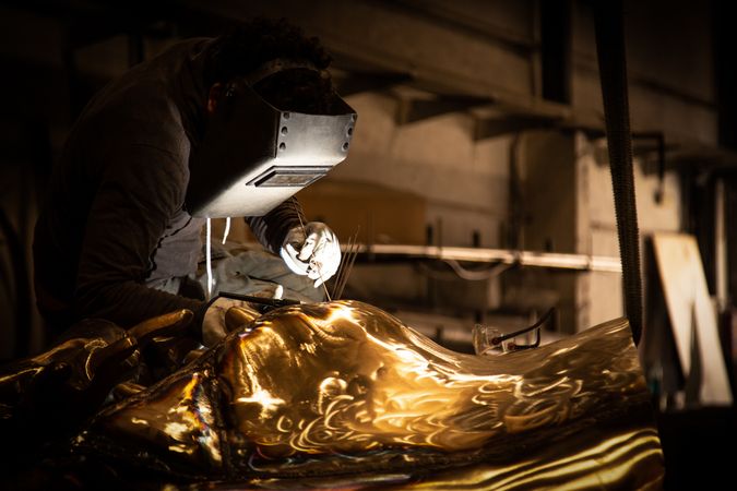 Man in mask welding metal ware in darkness