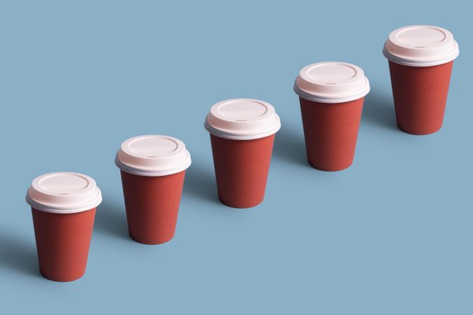 Single row of disposable coffee cups on blue background