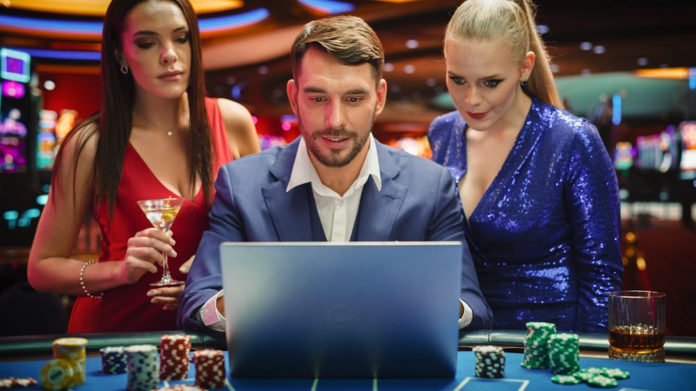 Portrait of a Happy Man with Two Female Partners Betting Online on a Laptop Computer while Sitting in a Luxury Casino.