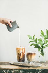 Hand pouring cream into iced coffee, vertical composition