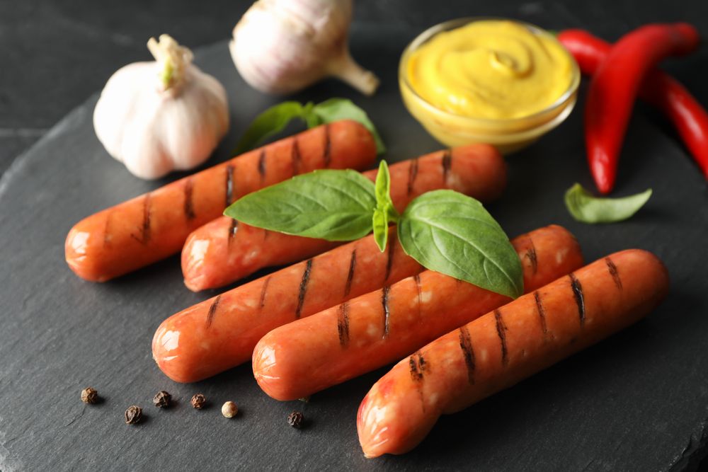 Grilled sausages or hot dogs on dark ceramic plate with garlic and mustard