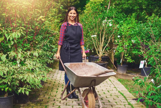 Smiling florist pictured with wheelbarrow in a greenhouse