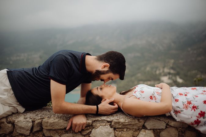 Affectionate couple resting while lying on stone fence in mountains