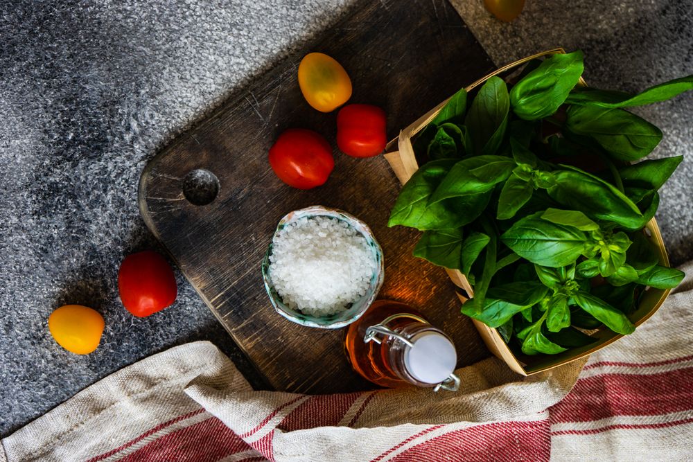 Top view of fresh basil, cherry tomatoes, salt and oil on bread board