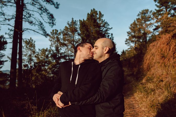 Smiling men hugging and kissing on path in park