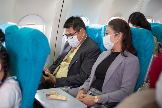 Male and female business professionals in facemasks on flight with snacks