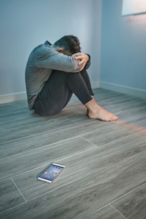 Man with problems sitting on the floor with mobile on the floor