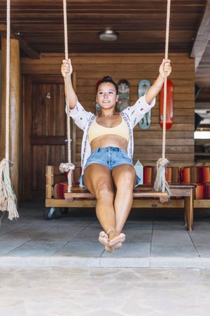 Cheerful woman riding on swings on tropical terrace
