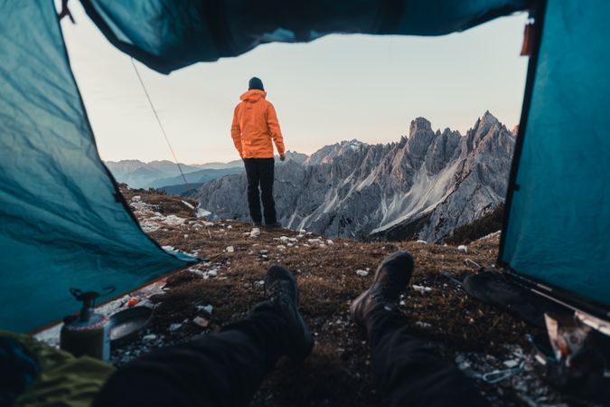 Cropped image of person in a tent looking at a person in orange jacket in mountain