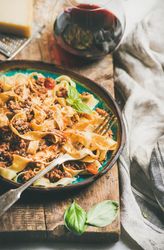 Pasta dinner with minced meat, cheese and red wine on wooden board, close up