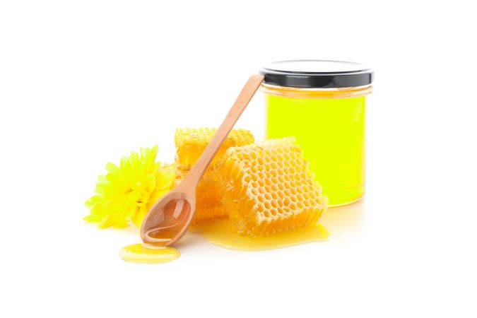 Pieces of honeycomb, glass jar, spoon and chrysanthemum isolated on plain background