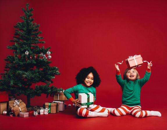 Two beautiful girls wearing holiday pajamas and sitting on floor with gifts