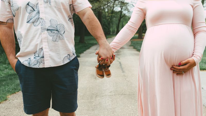 Pregnant woman and man holding hands and holding baby shoes outdoor