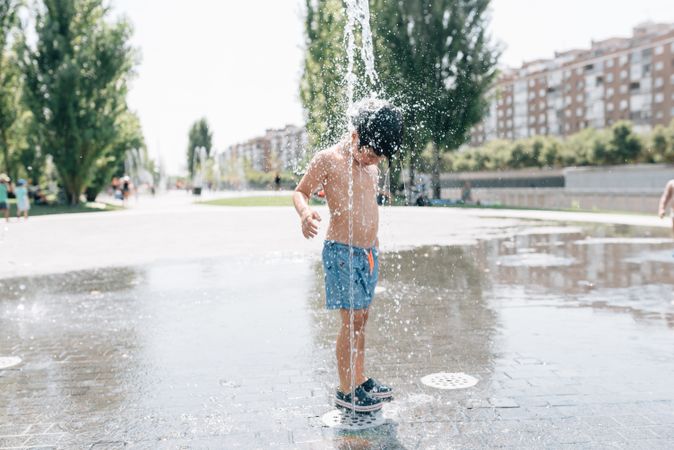 Kid standing in jet of fountain on street