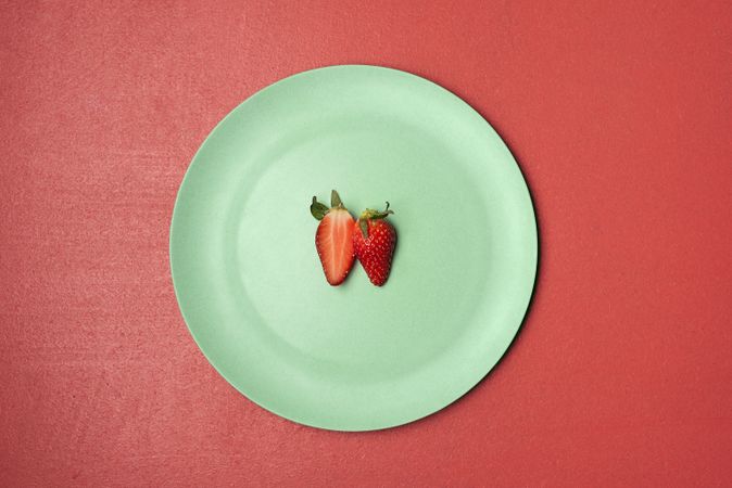 One strawberry cut in half on green plate
