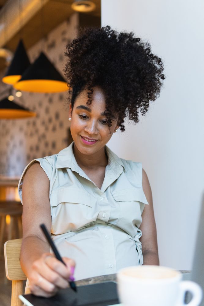 Smiling Black woman working on graphic tablet in cafe
