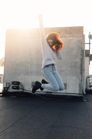 Red haired woman jumping for joy on roof