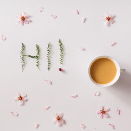 "Hi!" message made of green grass with cup of coffee or tea and flowers