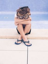 Frustrated kid in swimming glasses on pool border
